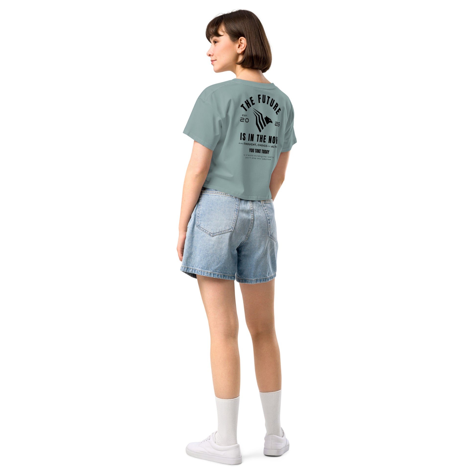 Person wearing a light green t-shirt with text on the back and denim shorts on a white background. Inspirational quote crop top — light, empowering, and bold.